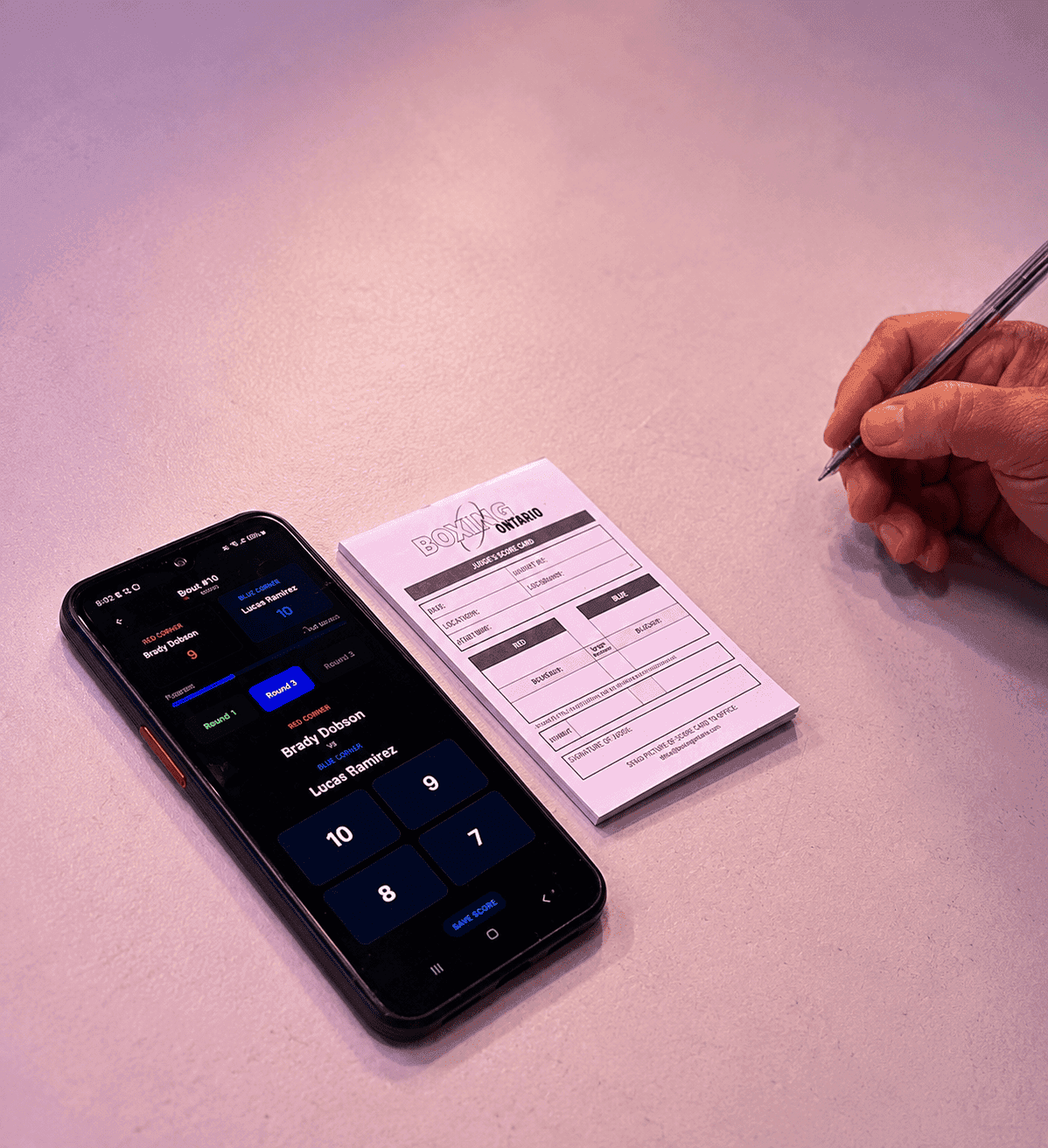 A phone running RingScore beside a paper boxing scorecard.